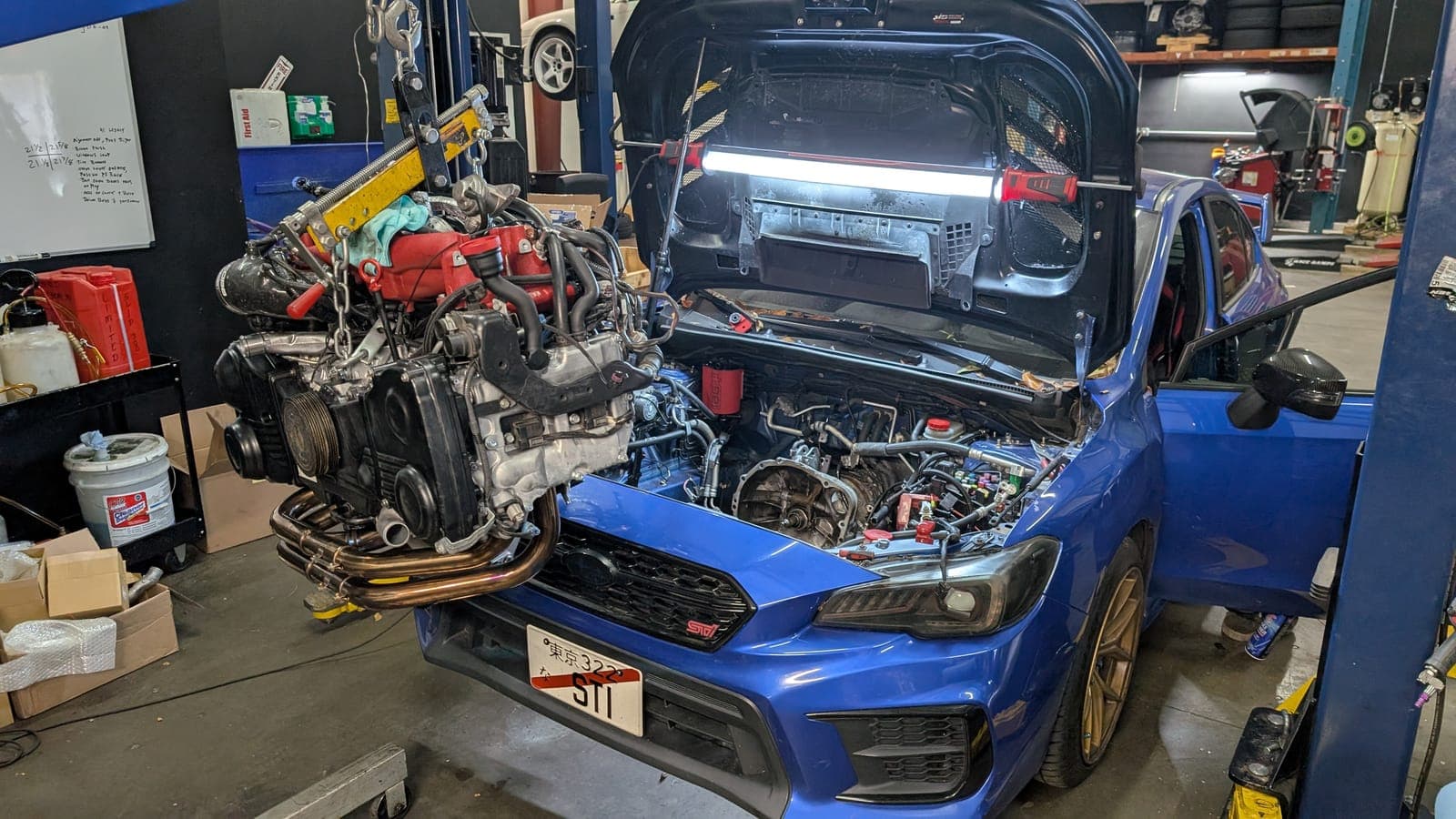 Blue Subaru WRX STI inside the Streamline Performance Garage shop with its boxer engine removed and hanging from an engine hoist