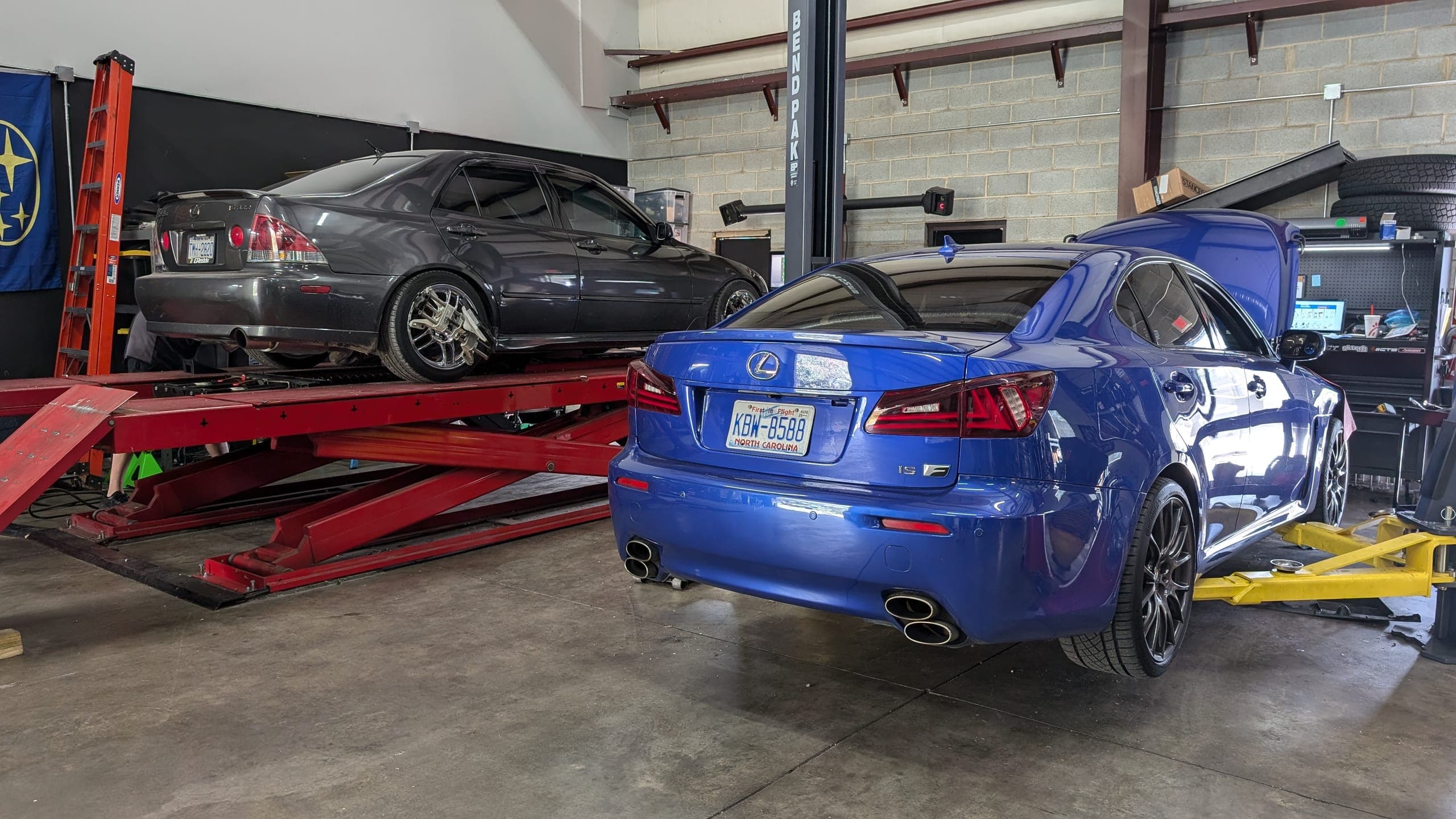 Blue Lexus IS F and a gray Lexus IS 300 on the alignment rack inside the Streamline Performance Garage shop in Concord, NC